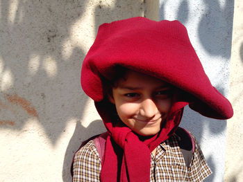 Portrait of schoolboy with red sweater on head against wall