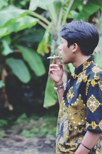 Young man holding cigarette while standing outdoors