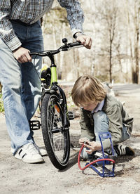 Boy filling bicycle tire with foot pump while father standing on road