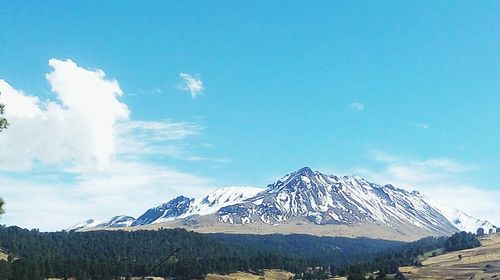 Scenic view of snow covered mountains against blue sky