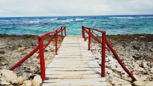 Wooden railing on beach against sky