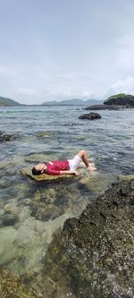 Woman lying on rock in sea against sky