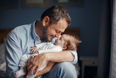 Smiling father rubbing nose of baby daughter at home