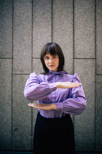 Portrait of young woman gesturing while standing against wall