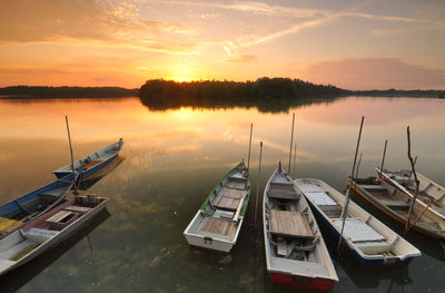 Boats moored in calm lake at sunset