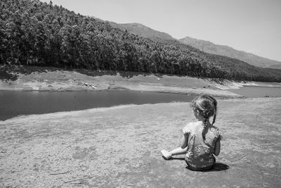 Full length of girl sitting by lake against sky