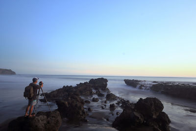 Rear view of woman standing at beach against clear sky