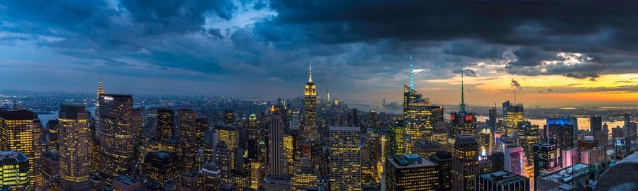 Panoramic view of illuminated cityscape against dramatic sky