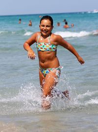 Portrait of smiling girl wearing swimwear walking in sea