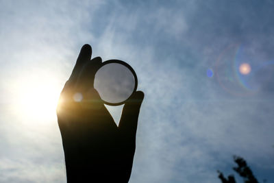 Cropped hand holding crystal ball against sky