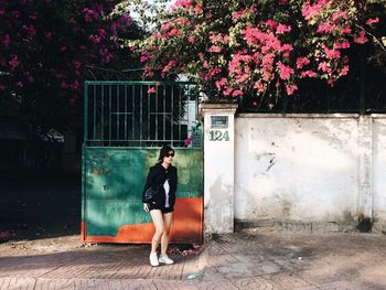 Full length of young woman standing on footpath against retaining wall