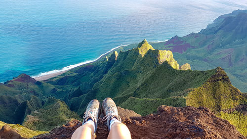 Low section of woman legs by sea against mountain