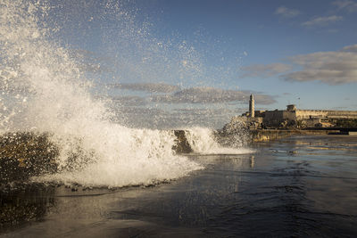 Sea waves splashing on shore against sky