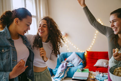 Happy female friends enjoying while singing together at home