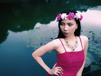 Beautiful young woman wearing flowers against lake