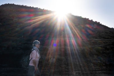 Man standing in forest against bright sun