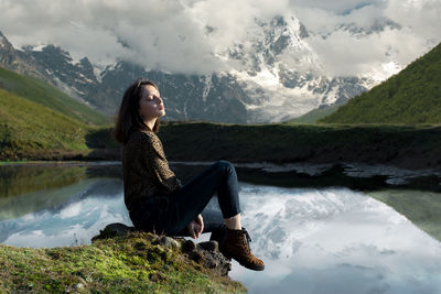Georgian girl sits near the lake and around is beautiful nature