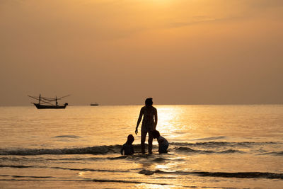 Silhouette mother with children standing in sea during sunset