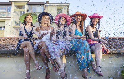 Low angle view of female friends throwing confetti while sitting on roof