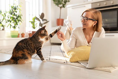 Happy woman freelancer lying on carpet in living room, plays with cat a toy mouse at home. love pets