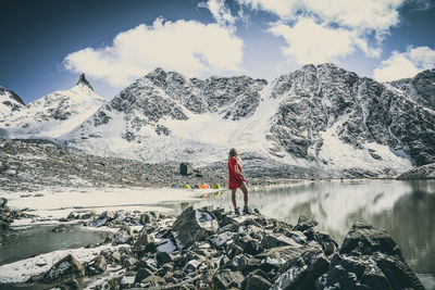 Rear view of woman standing against snowcapped mountains on rock