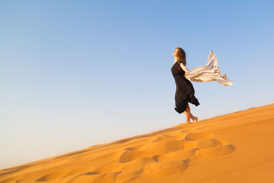 Woman standing on sand against clear sky