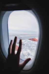 Cropped hand on airplane window against aircraft wing