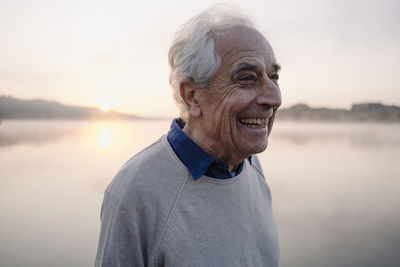 Happy man looking away while standing against lake