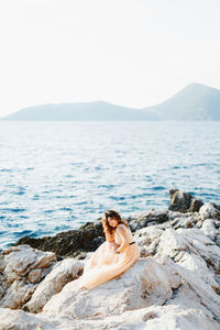 Full length of woman sitting on rock against sea