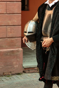 Midsection of man holding umbrella standing against brick wall