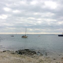 Boats in calm sea against cloudy sky