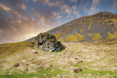 Close-up of rock formation on grass under mountain against sky during sunset