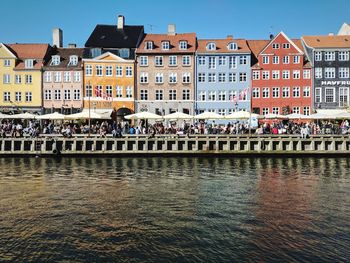 People on river by buildings in city against sky