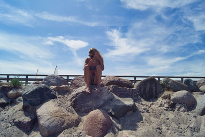 Young woman sitting on rock by sea against sky