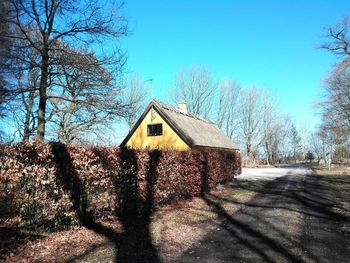House amidst bare trees and buildings against sky