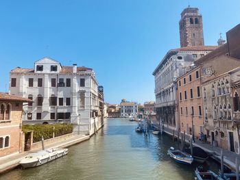 Canal passing through buildings against blue sky