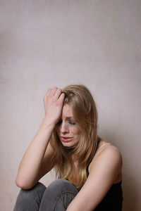 Woman sitting and crying against wall