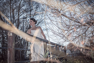 Woman standing by bare tree against sky