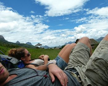 Male and female hikers relaxing on field against sky