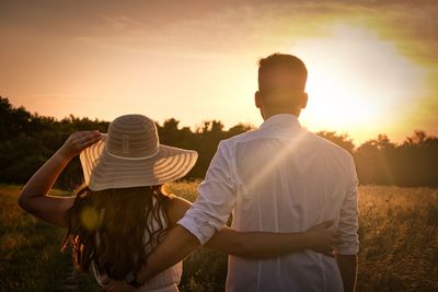 Rear view of couple standing on field against sky during sunset