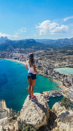 Woman standing on rock by sea against sky