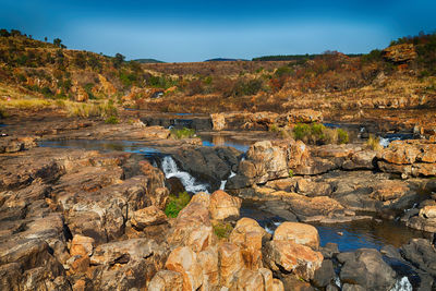 Rocks by river against sky