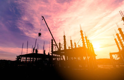 Silhouette cranes at commercial dock against sky during sunset