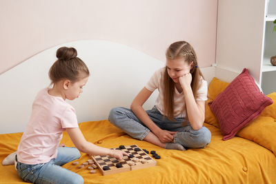 Sisters playing draughts board game on bed