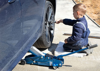 A little boy fixes a car, changes a wheel, helps his dad.
