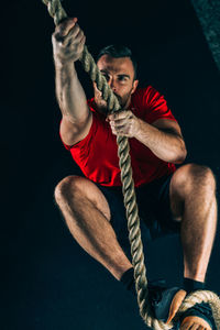 High angle view of male athlete climbing on rope in gym