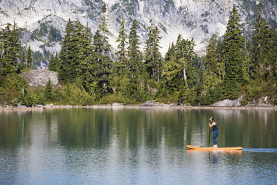 Side view of active woman paddle boarding on mountain lake.