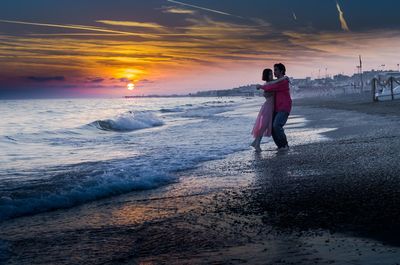 People on beach against sky during sunset