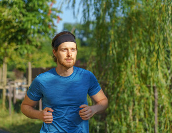 Athletic european man in sportswear jogging on road in green park on beautiful summer day