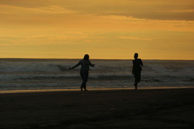 Silhouette people on beach against sky during sunset